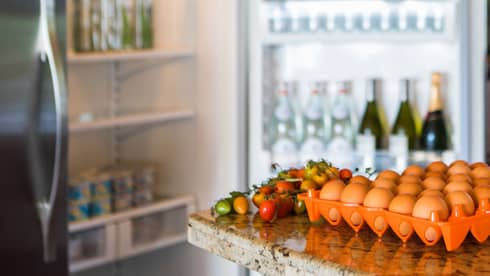 Smiling man holds green bottle in front of open fridge, fresh eggs on counter