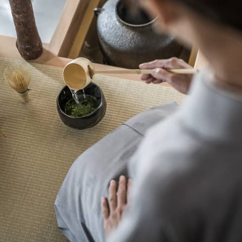 Woman kneels and pours tea from ladle during Tea Ceremony
