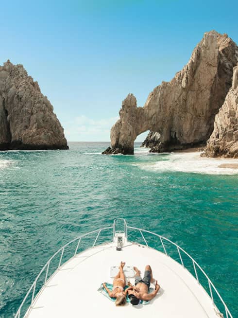 Two people lie on the front of a boat in Cabo