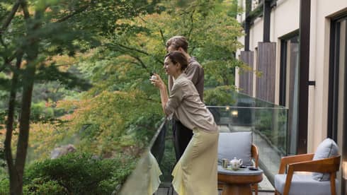 Two people enjoying a peaceful moment on a balcony surrounded by lush green trees at Four Seasons
