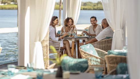 Four friends dine poolside at Bambou under a cabana