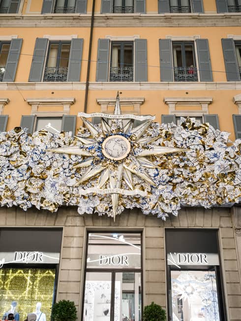 The front of a building in a city with a dazzling sculptural piece of artwork over a row of doors and windows.