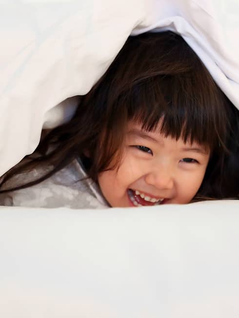 Young girl laughing as she plays under a white bed sheet