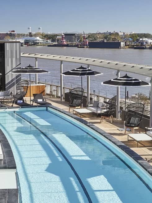 Rectangular pool with cabanas and lounge chairs with a view of the ocean.