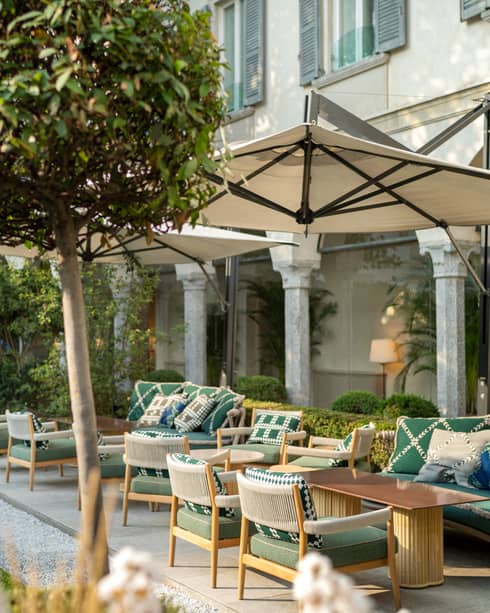 An outdoor seating area with umbrellas and green chairs surrounded by small trees.