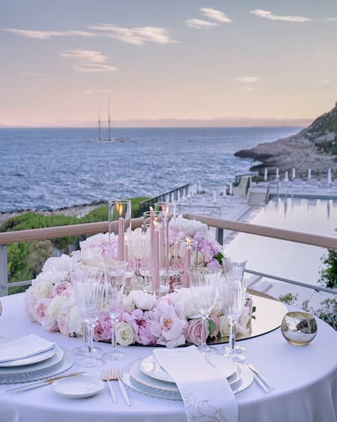 Balcony with round set table, pink floral arrangement, water views at sunset