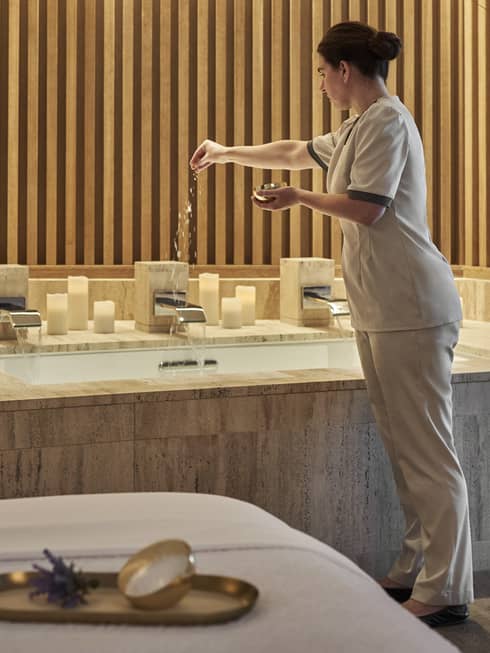 Person putting bath salts in a Spa tub with candles and a plant on the Spa tub.