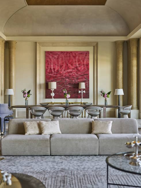 Grand hotel suite living room with pillars, a modern sofa and a large dining table set next to red artwork