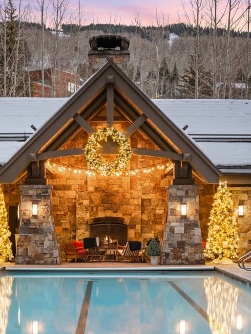 Cabin with two Christmas trees and an outdoor pool with a sunset in the background.