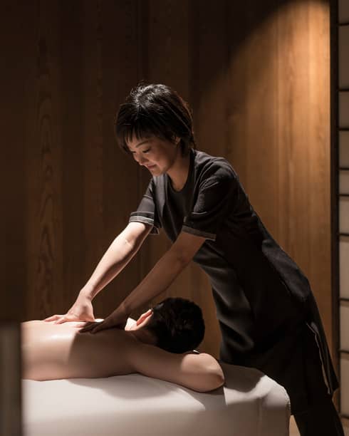Man lies face-down on massage table as masseuse in black uniform rubs his shoulders