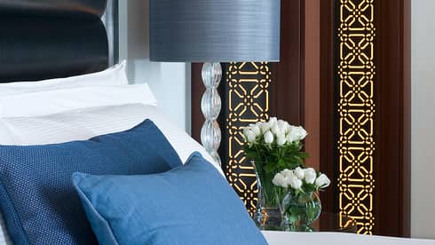 Close-up of bed with two blue pillows, glass lamp, decorative gold on wood panel