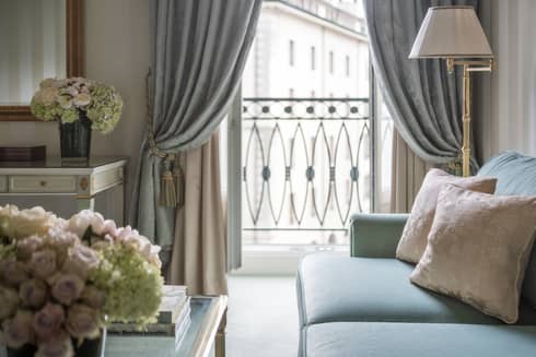 Close-up of blue sofa, two cream accent pillows, white and gold lamp, sunny French balcony in background