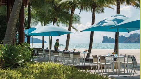 Server sets patio dining tables under blue umbrellas along beach 