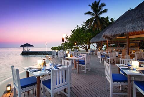 Reef Club on the water at sunset, with white tables on open patio and torches 