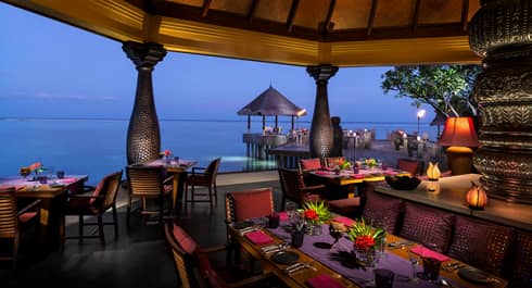 Evening view of Baraabaru restaurant dining patio on the water, with tropical flower arrangements, lanterns