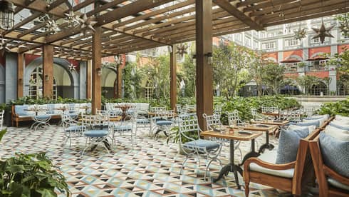 Colourful tiles, iron patio chairs with blue cushions, tables under awning on Zanaya terrace
