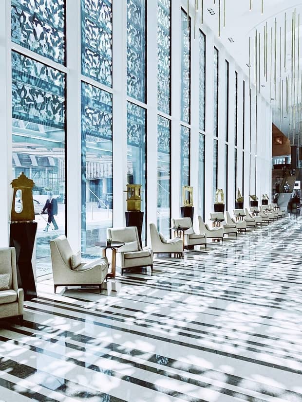 Lobby with soaring windows reflecting floral patterns over marble floors, armchairs and tables