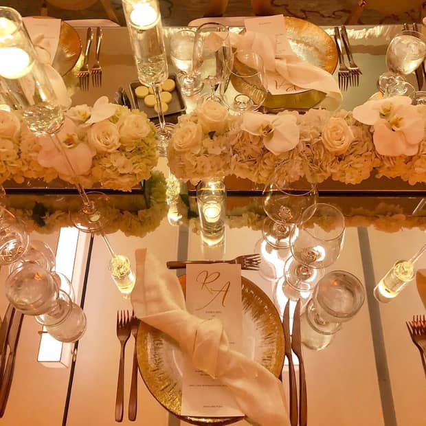 Wedding dining tables, menu and napkin on plate surrounded by glassware, cream coloured flowers, candles