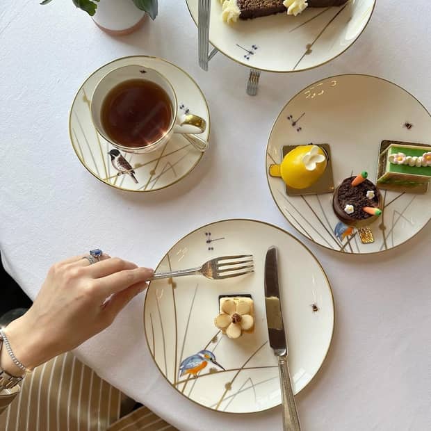 Aerial view of an afternoon tea spread of hot tea and petits fours, served on cream-colored glass plates with birds on them