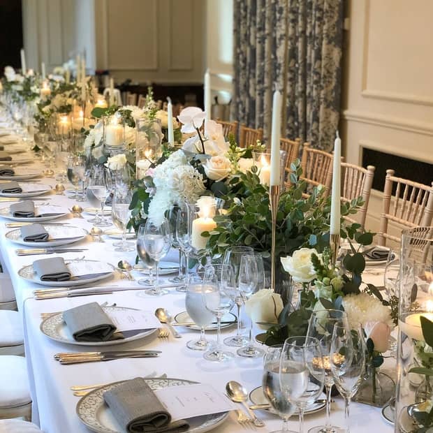 Wedding dining table arrangement with floral bouquets, candles and plates