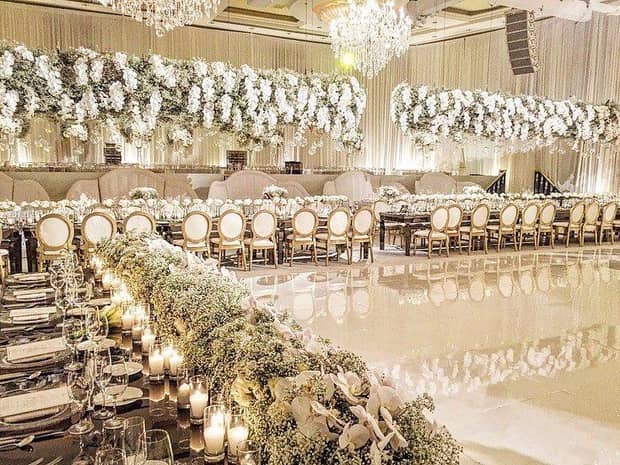 A wedding reception area with hanging flowers, flowers on long tables, and white and gold chairs surrounding a large floor.