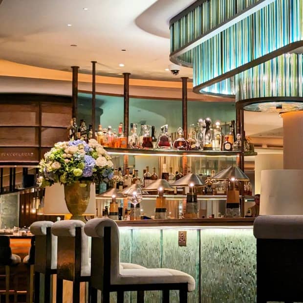 A bar with modern decor and bright lighting, decorated with metal table lamps and a large floral arrangement