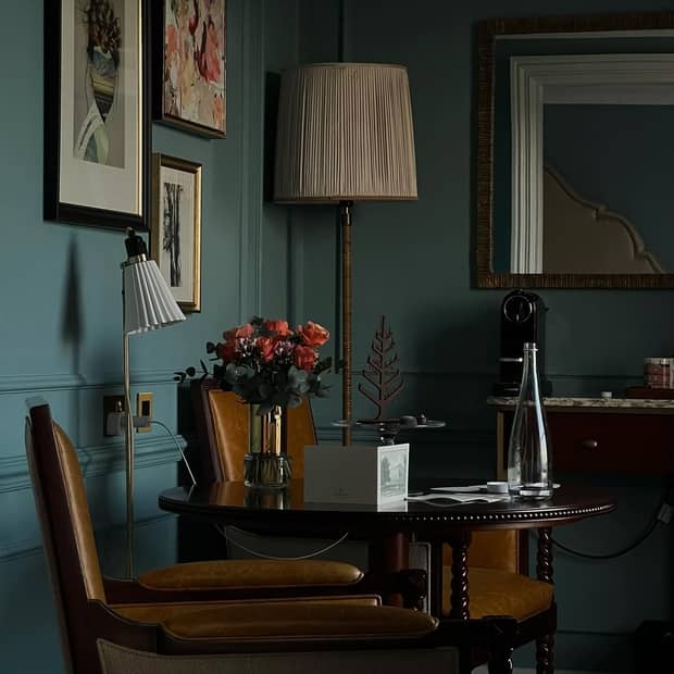 The corner of a guest room with two leather chairs and a wooden table in front of a blue wall with framed artwork
