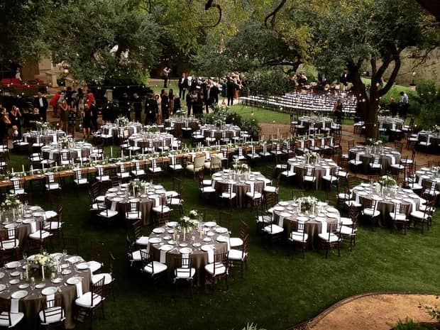 Outdoor garden wedding reception, guests gather on patio behind rows of banquet tables