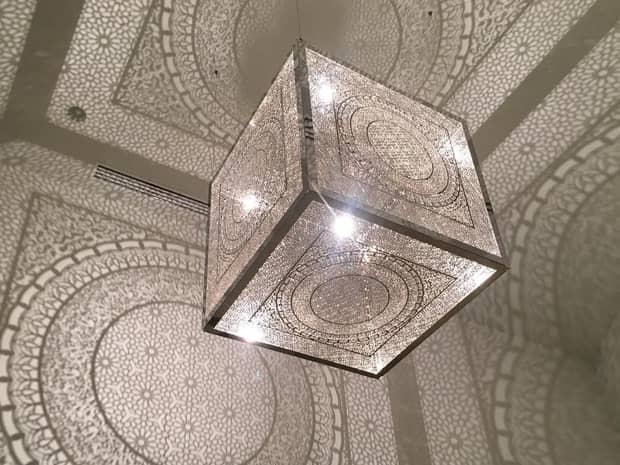 Large cube lantern chandelier with intricate design casting shadows across ceiling