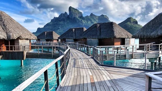 Wood bridge leading to overwater bungalow cottages over turquoise Bora Bora lagoon