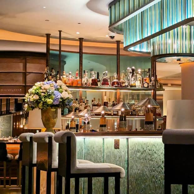 A bar with modern decor and bright lighting, decorated with metal table lamps and a large floral arrangement