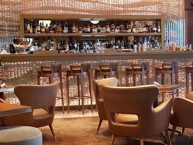 Retro-style wingback cocktail lounge chairs by bar with lights, stools