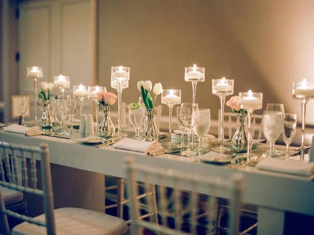 Close-up of long, elegant banquet dining table with tealight candles in tall glass holders