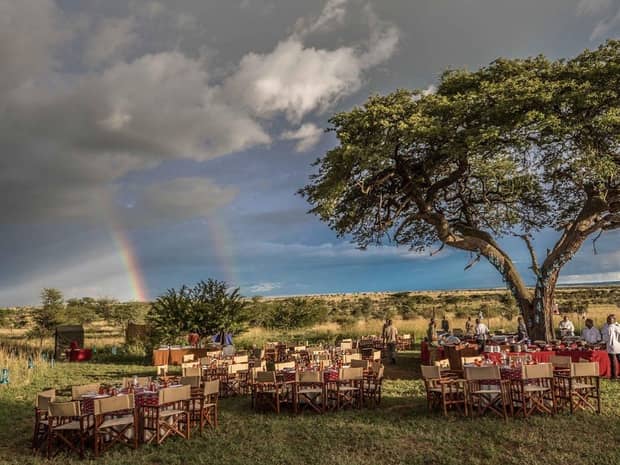 Double rainbow in sky over outdoor wedding reception on event lawn under tree