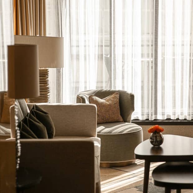The corner of a hotel suite with a linen sofa and chair, stackable wooden side tables and modern decor
