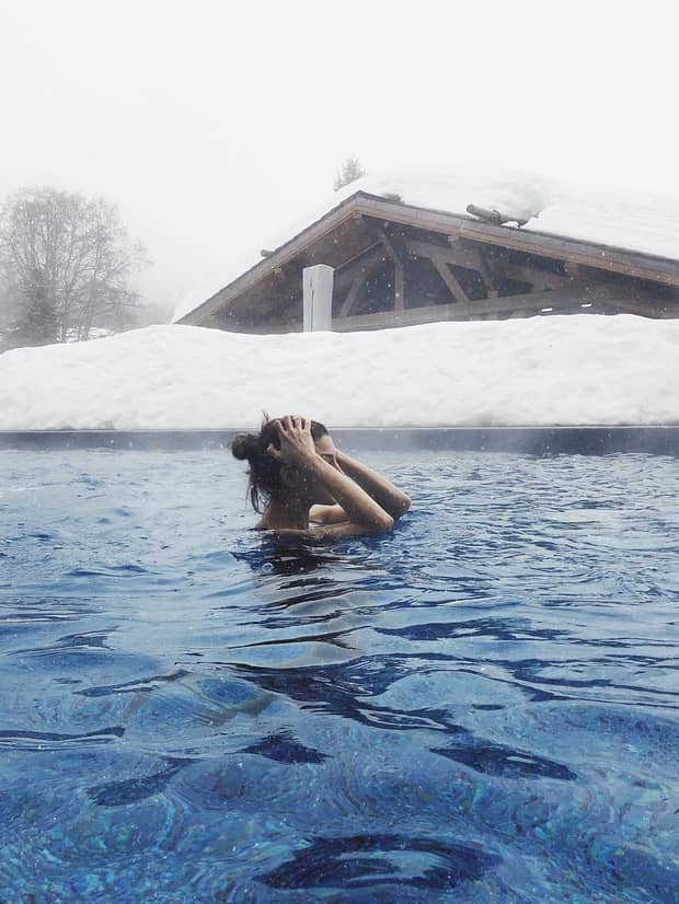 Winter swim, woman wades in outdoor heated pool under snowy deck