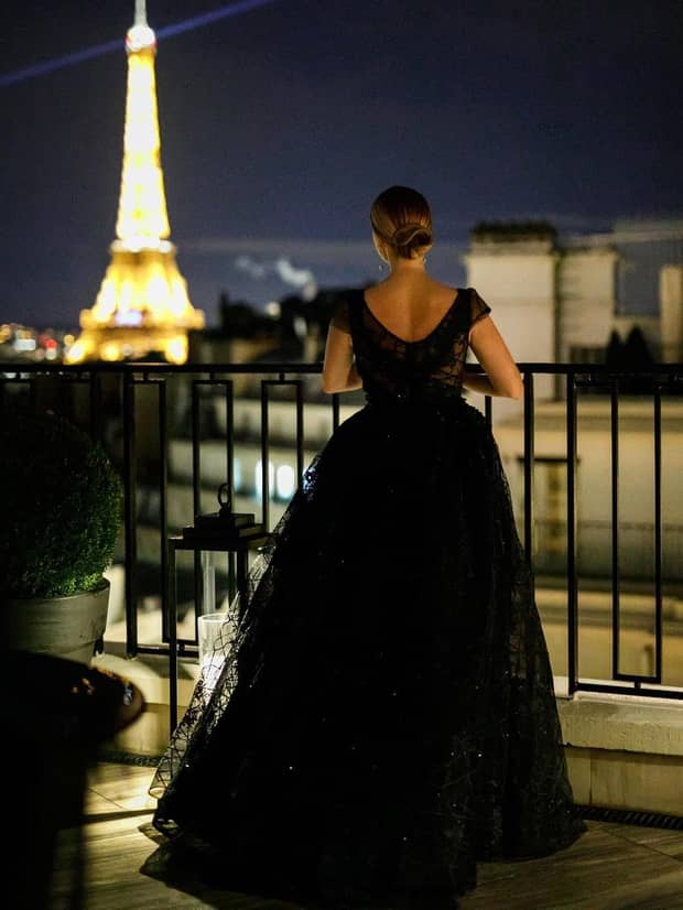 Person in black dress on balcony looking out at Eiffel Tower outside luxury hotel event rooms