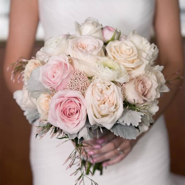 Bride in wedding gown holds pink and white bouquet of roses