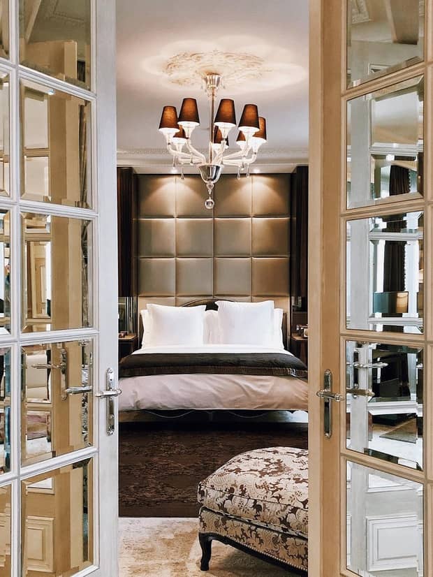 View through French doors to bed under large padded headboard