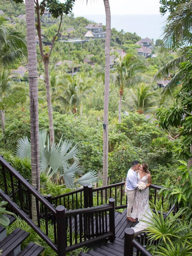 Bride and groom kiss on outdoor staircase landing, tropical forests in background