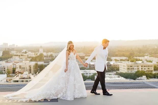 Bride and groom walk across roof as sun sets over Los Angeles