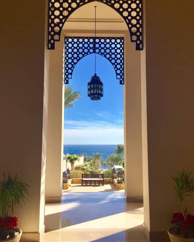 Sea, sunny patio visible beyond tall arched doorway with hanging lantern