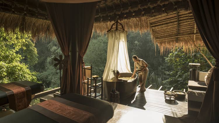 Hotel staff greets woman in spa bath tub in outdoor treatment room