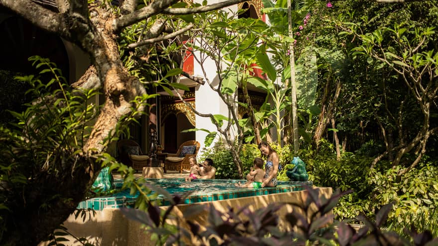 Family relaxing in a private plunge pool surrounded by tropical plants and traditional architectural details.