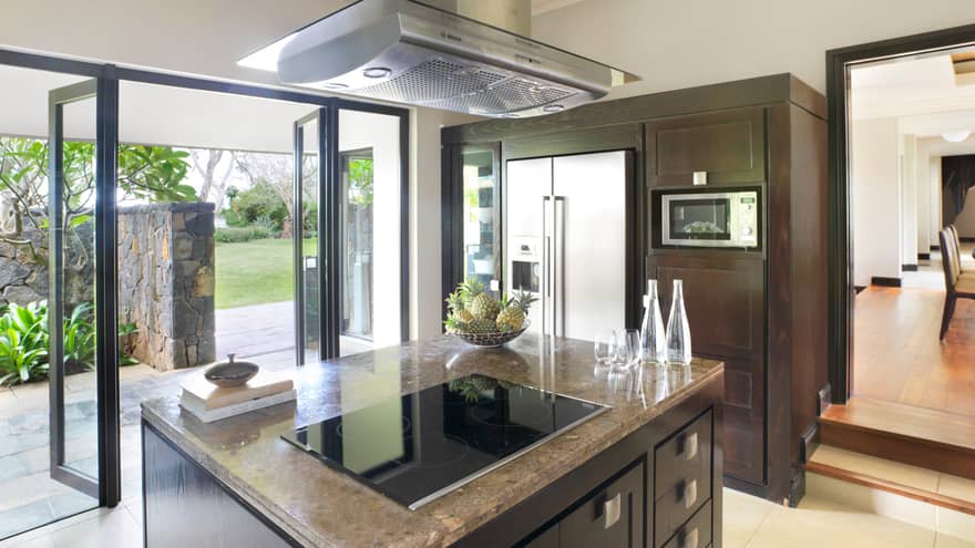Stove range on marble island in modern kitchen, open glass walls to patio