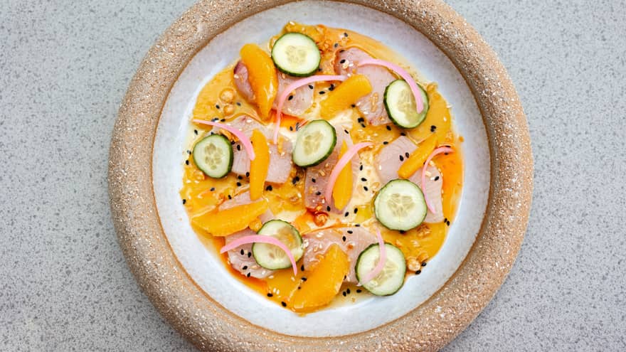 A round plate holds colourful food items, including citrus segments and cucumber slices.