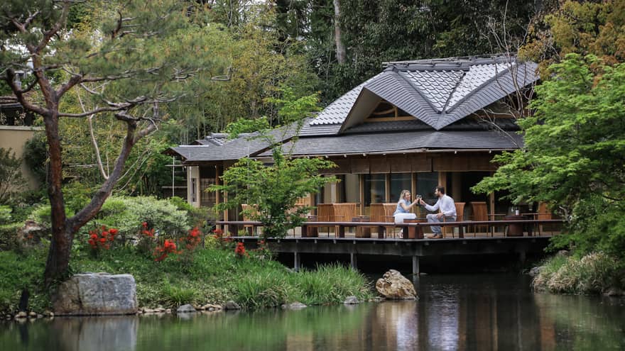 View across pond to restaurant patio where couple toasts with wine glasses
