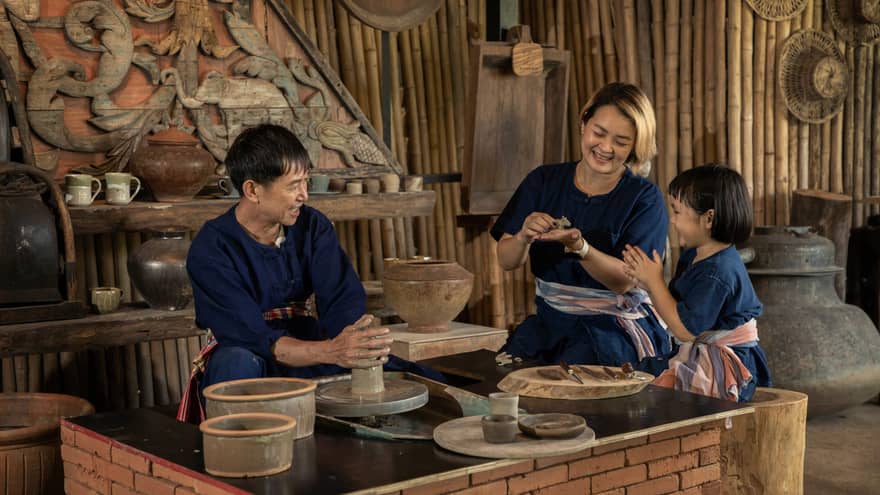 A potter teaching a woman and a child to shape clay in a rustic pottery workshop, surrounded by traditional tools and pottery.