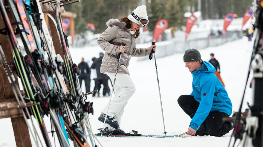 Hotel staff holds skis as woman holding poles steps in by ski rack, snowy hill