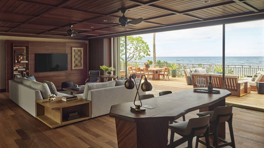 Wooden desk and living room with light grey sofa, full wall of windows with ocean view